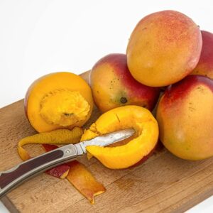 Sliced and whole mangoes on a wooden board with a knife, showcasing vibrant fruit freshness.