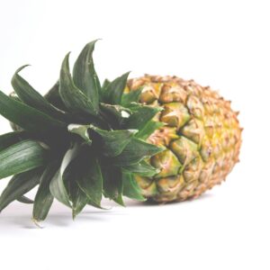 A single ripe pineapple with vibrant green leaves set against a white background, showcasing freshness.